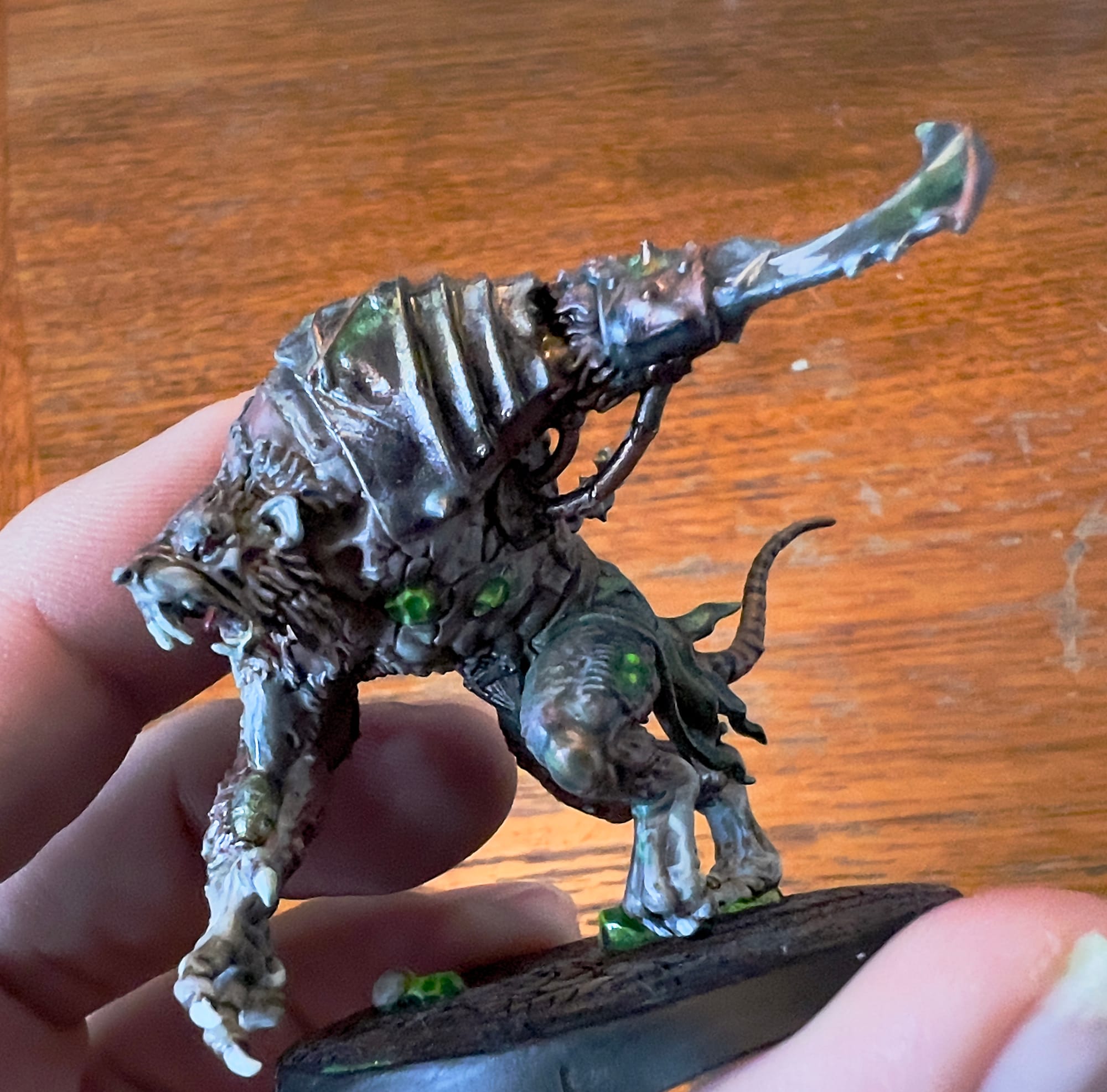 Close-up of a painted rat-like mutant miniature with glowing green pustules, metal armour plates, and a raised bladed arm, standing on a cracked dark base.