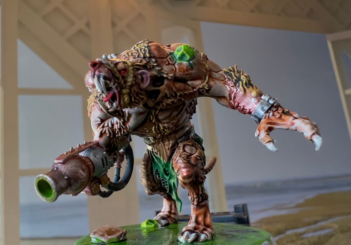 Painted miniature of a mutated rat-like creature with a large claw, metal arm cannon, and glowing green boils, standing snarling on a slime-covered base.