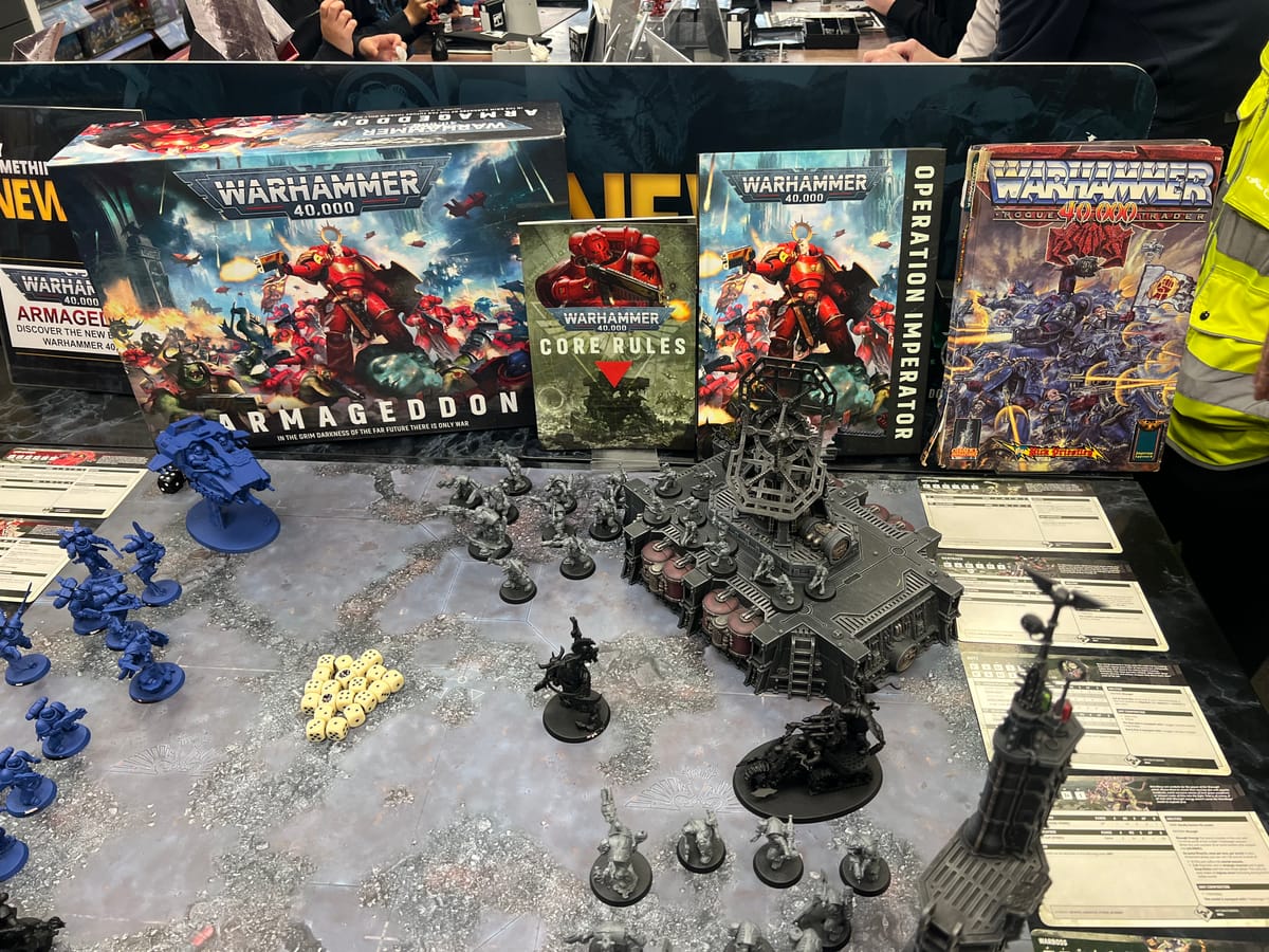 Warhammer 40,000 display table with miniatures, terrain and dice, showcasing modern books beside the original Rogue Trader rulebook.
