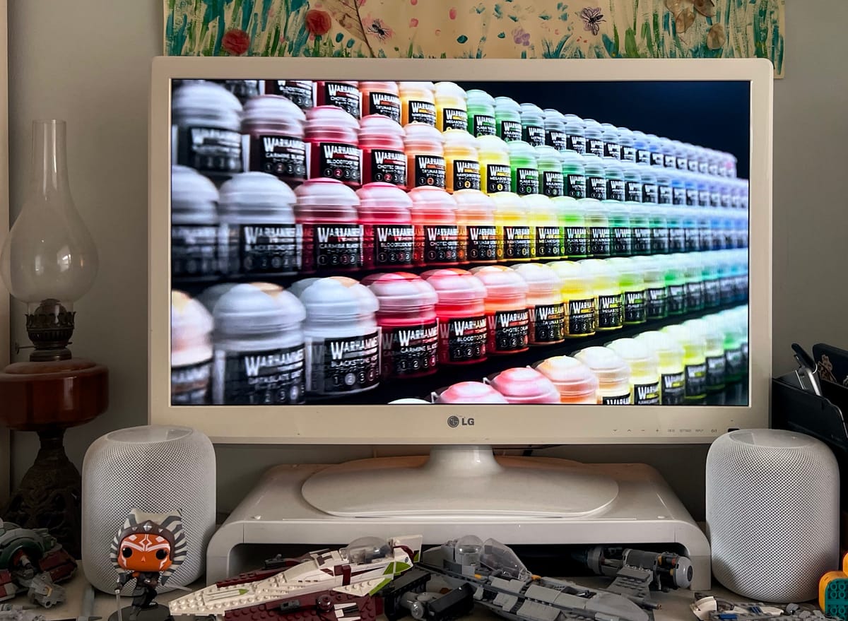 An old LG TV showing the Warhammer Autumn Preview 2026 on the screen. Two white HomePods, and an Ashoka Funko Pop and an old oil lamp are visible.
