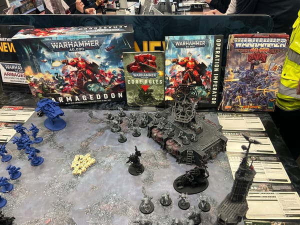 Warhammer 40,000 display table with miniatures, terrain and dice, showcasing modern books beside the original Rogue Trader rulebook.